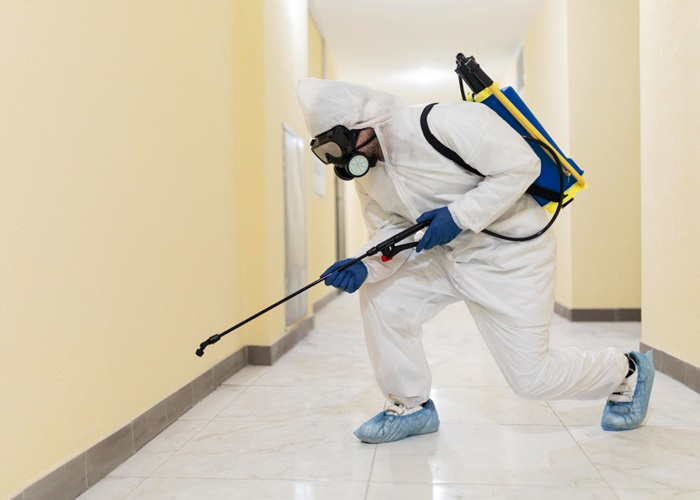 Pest control worker in a hazmat suit applying pesticide indoors.