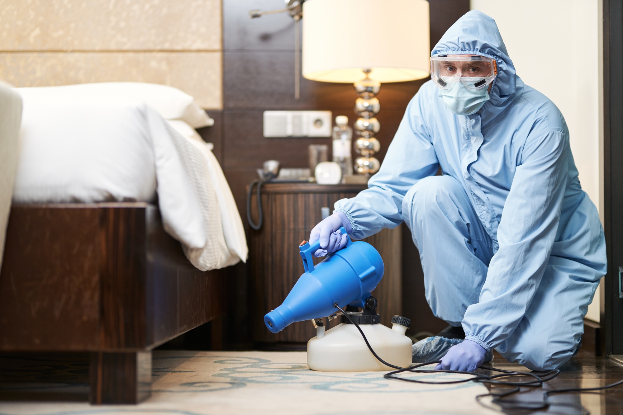 Man doing disinfection under the bed in a hotel room. Coronavirus and quarantine concept