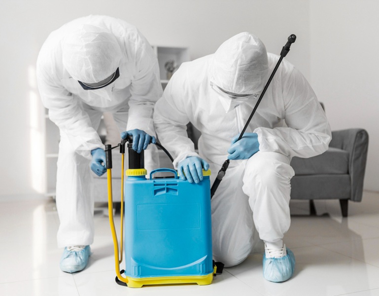 A pest control professionals wearing a full white protective (hazmat) suit, respirator mask, and goggles, holding sprayer wand, ready to apply pest control treatment.